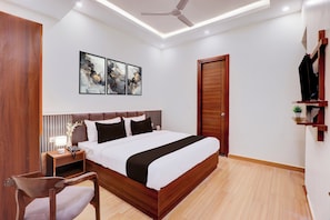 Une chambre moderne avec un lit en bois, une table de chevet avec une lampe, une chaise, un ventilateur de plafond et des œuvres d’art accrochées au mur.