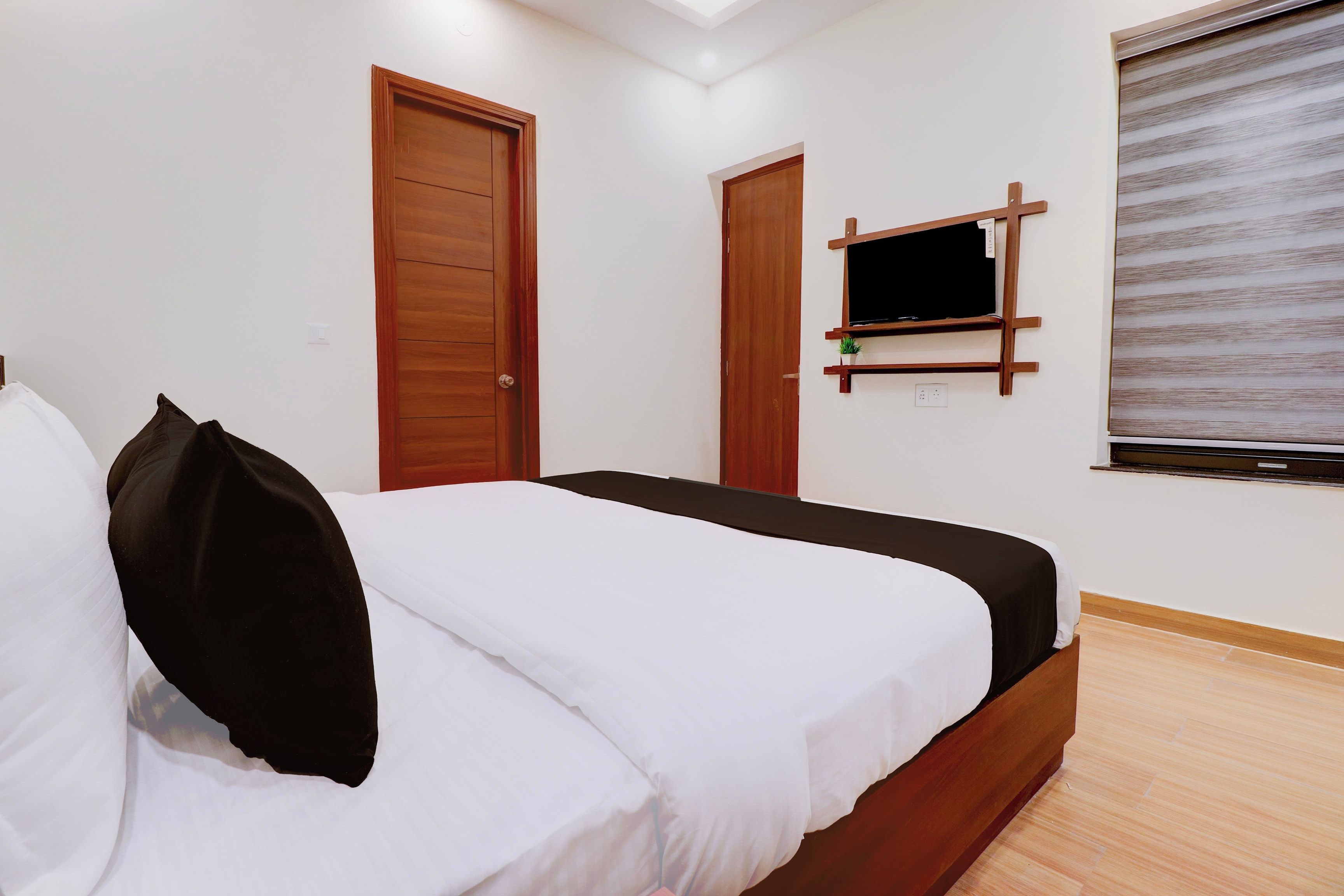 Quarto de hotel com cama, duas portas, televisão presa na parede e janela com persianas.