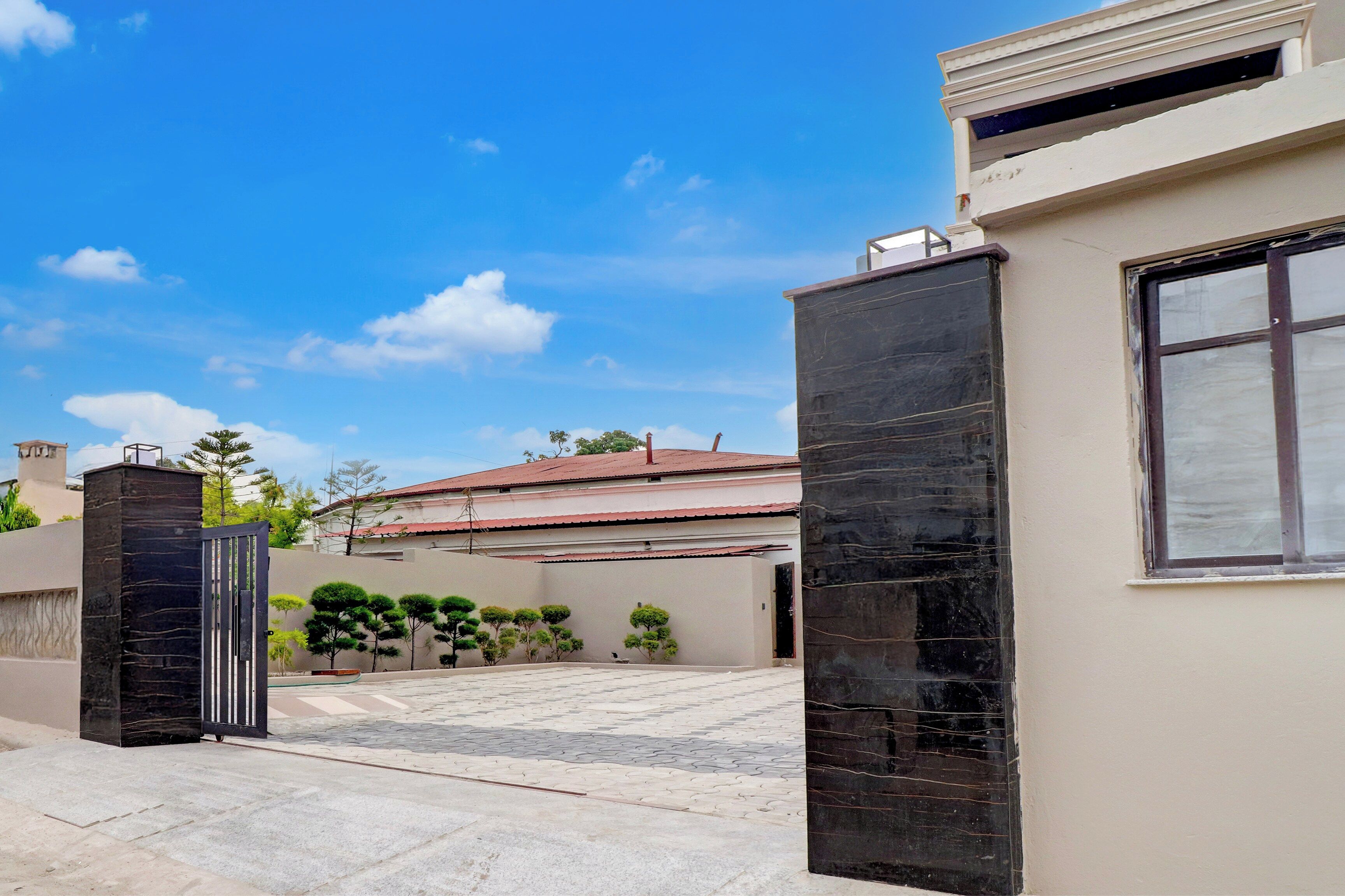 A gated entrance with a paved driveway leading to a building with a red roof.