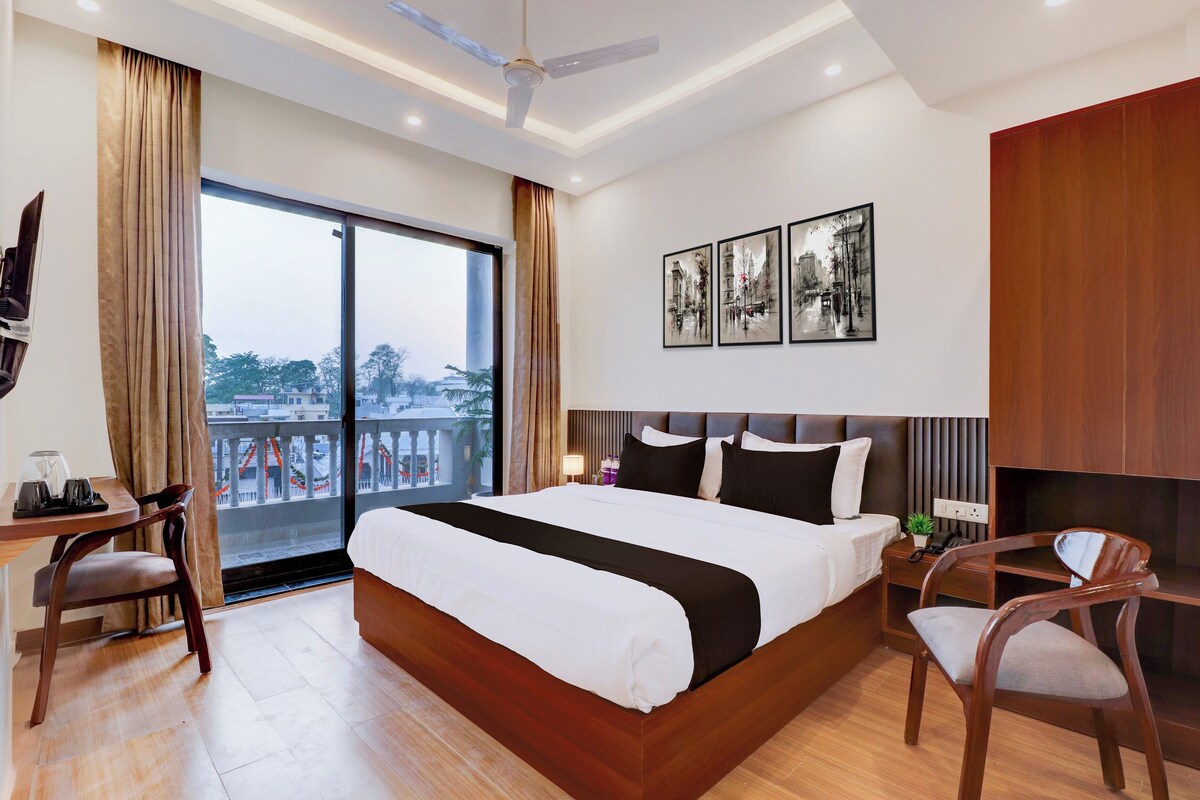 Une chambre d’hôtel avec un grand lit, un bureau avec une chaise, une table de chevet avec une lampe et une vue sur l’extérieur.