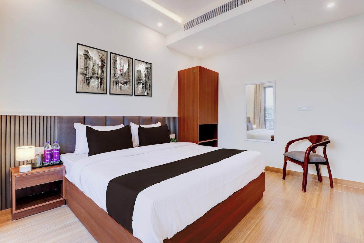 Une chambre d’hôtel moderne avec un grand lit, une table de chevet, une armoire en bois, une chaise et des œuvres d’art accrochées au mur.