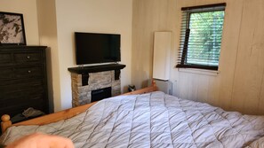 Una camera da letto con un letto, una televisione sopra un camino in pietra, un comò e una finestra con persiane.