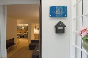 A hotel room with a bed, a small seating area, a TV, a kitchen area visible through an open door, and a wall-mounted sign. - Filo Guesthouse (Roma)