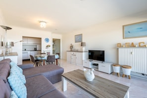 A modern living room with a sofa, coffee table, and a TV. There is a dining area with a table and chairs. The room has a kitchen in the background. - Apartment in Blankenberge by the North Sea (Blankenberge)