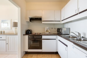 A compact kitchen with white cabinets, a built-in oven, a microwave, and a sink. - Apartment in Blankenberge by the North Sea (Blankenberge)