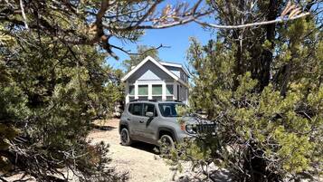 Un véhicule est garé dans un environnement naturel, avec une maison en arrière-plan.