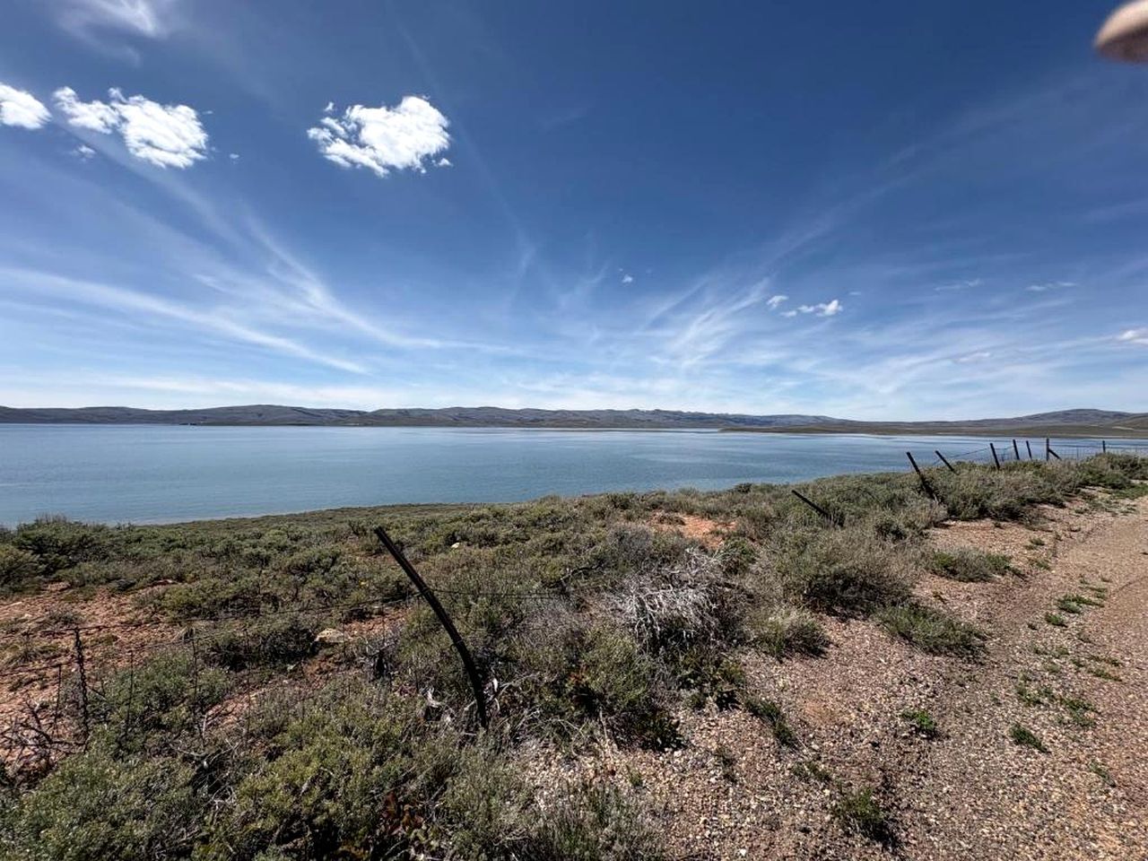 Un paysage naturel caractérisé par un ciel dégagé, une étendue d’eau et une zone délimitée par une clôture, où la végétation est clairsemée.