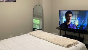 Un dormitorio con cama, televisor, espejo y un cuadro en la pared.