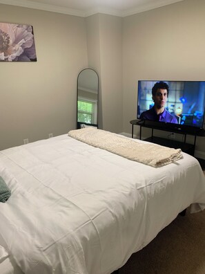 Een slaapkamer met een bed, een televisie, een spiegel en een schilderij aan de muur.