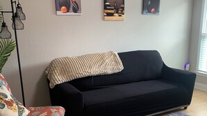 Una sala de estar con un sofá negro, un sillón estampado y un tapete gris. Hay tres obras de arte colgadas en la pared sobre el sofá.