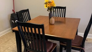 Una mesa de comedor con cuatro sillas, un jarrón con flores y un trapeador rojo al fondo.