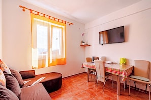 A cozy living room with a sofa, a dining table with chairs, a TV mounted on the wall, and a window with curtains. - A2 - Apartment 50m from the beach with the sea view (Korcula)