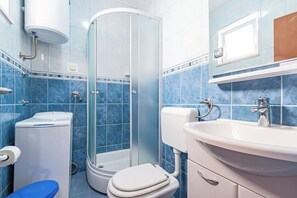 Et badeværelse med brusekabine i glas, toilet og et spejl over vasken.