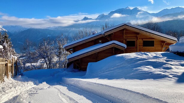 A wooden cabin with a sloped roof, surrounded by snow-covered landscape and mountains in the background. - Vrbo Property (Combloux)
