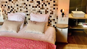 A bedroom with a checkered headboard, a bed with two pillows, a bedside table with a lamp, and a bathroom with a sink and mirror. - Vrbo Property (Combloux)
