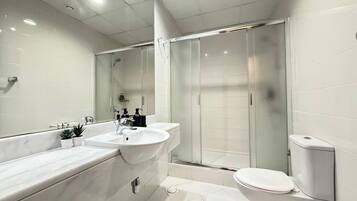 A modern bathroom with a large mirror, two sinks, a shower enclosure, and a toilet.