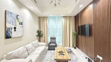 A modern living room with a sofa, armchair, coffee table, and a flat-screen TV mounted on the wall.