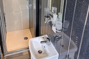 A bathroom with a glass shower enclosure, a sink with a chrome faucet, and toiletries on the wall. - Cabin Sleeps 2 With Heating (Mablethorpe)