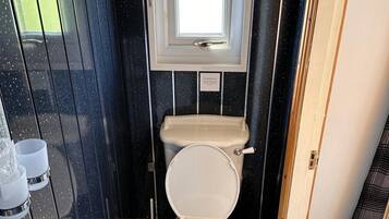 Un baño pequeño con inodoro, ventana y zona de ducha.