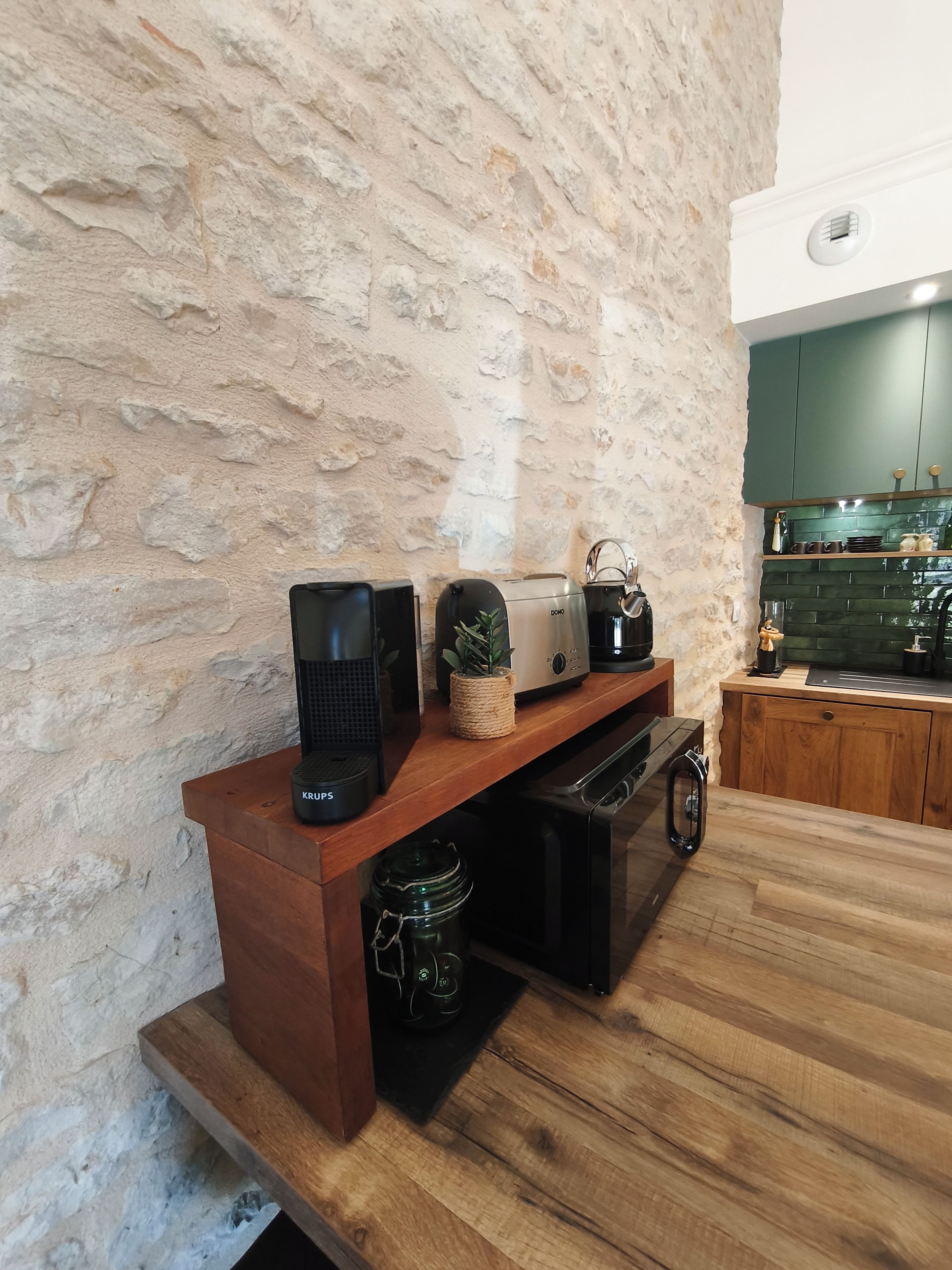 A kitchen with a stone wall, wooden countertop, and various appliances including a coffee maker and a toaster.