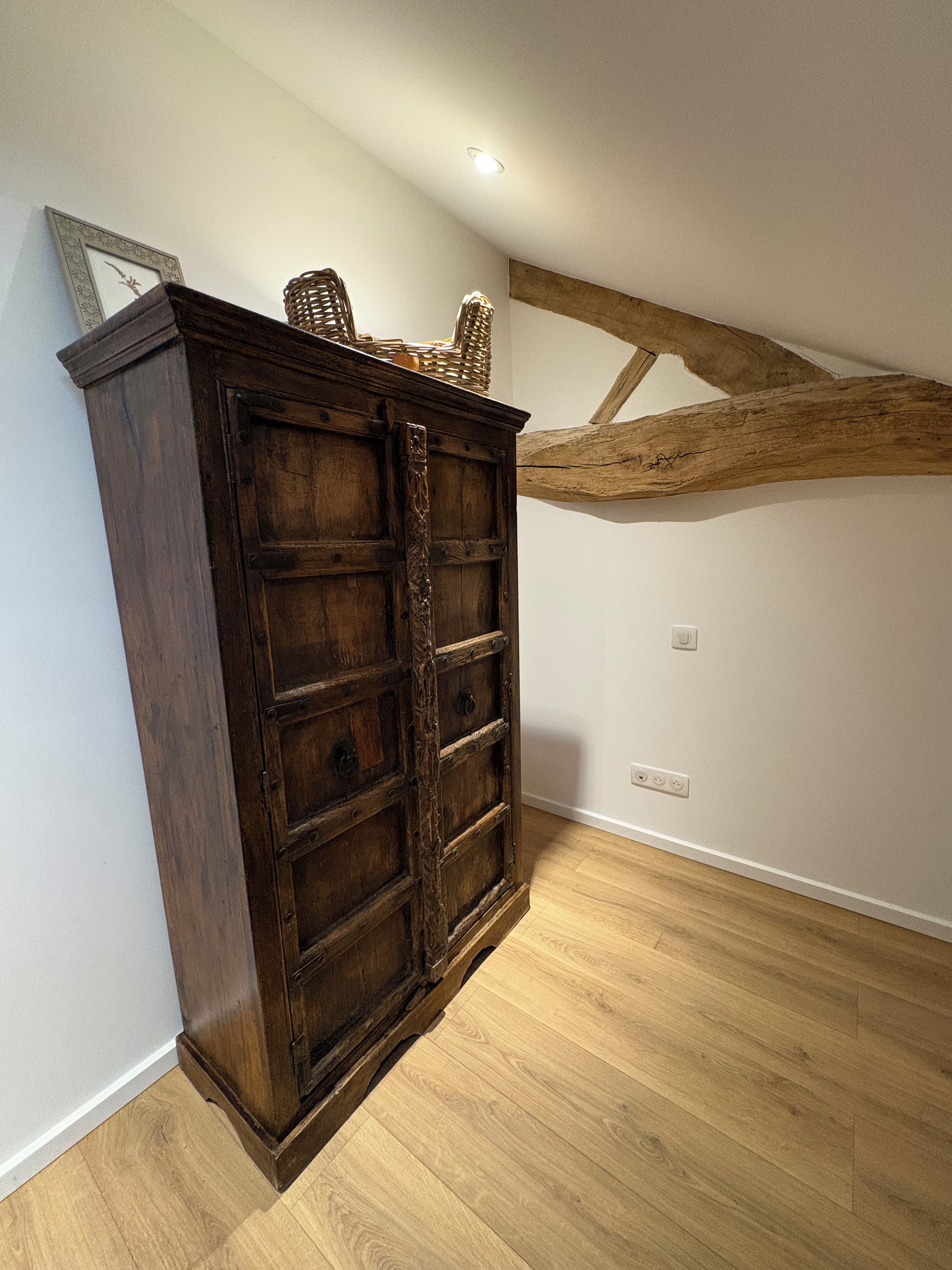 Un gabinete de madera con una puerta grande, una cesta tejida encima y un techo con vigas de madera.