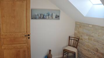 Um quarto com porta de madeira, parede de pedra, um vaso azul, uma cadeira de vime e um claraboia.