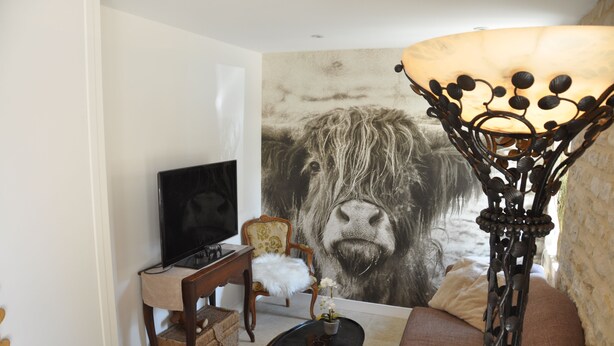 Una sala de estar con un gran mural de animales, un televisor, un sofá, una lámpara y una pequeña mesa con un jarrón.