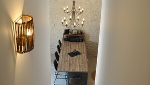 Un comedor con mesa de madera, sillas, una lámpara de araña y pared de piedra.