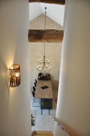 Een eetruimte met een houten tafel, stoelen, een kroonluchter en een stenen muur.