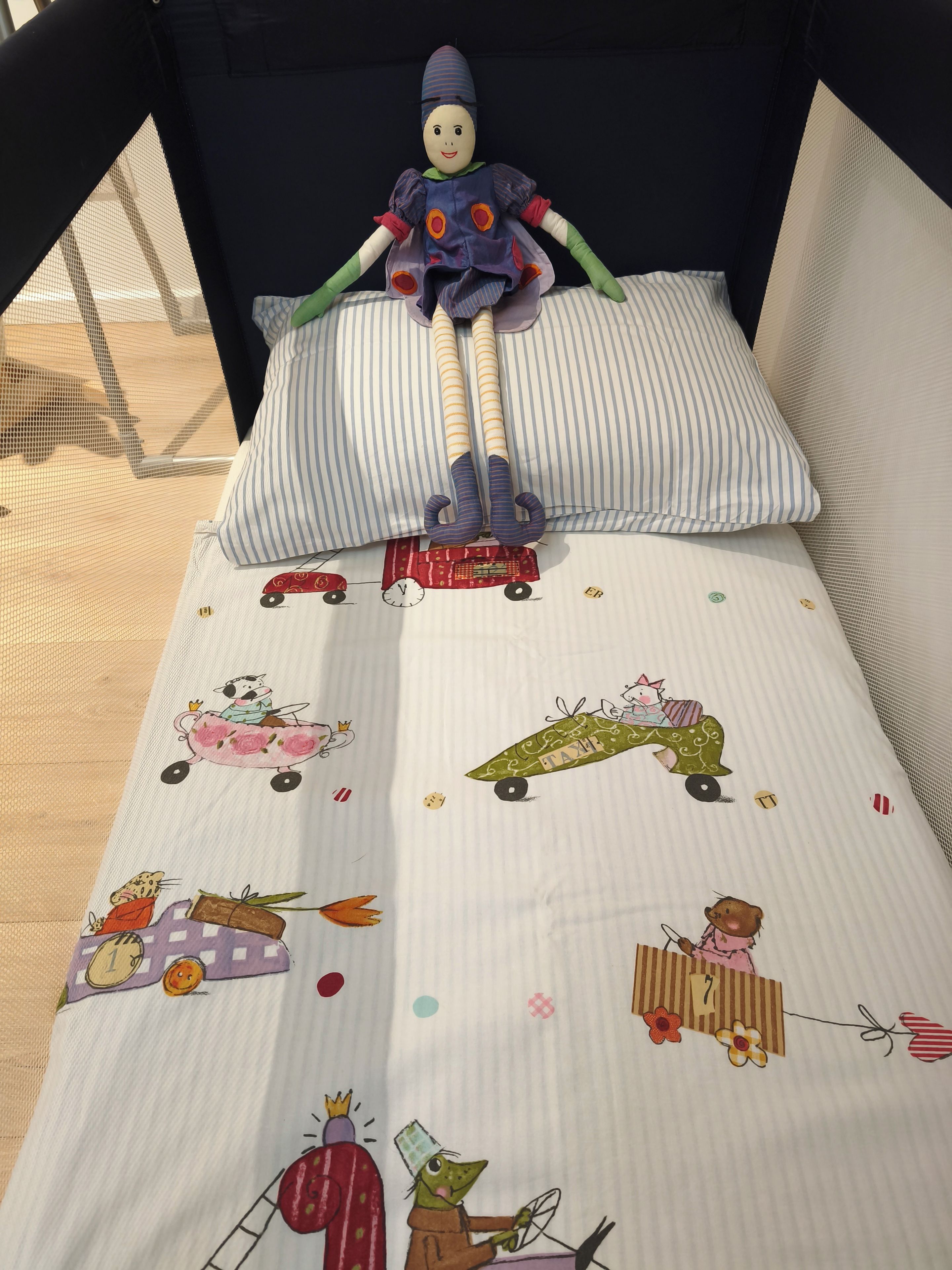 Una cuna con un muñeco, ropa de cama a rayas y un diseño alegre con animales y vehículos.