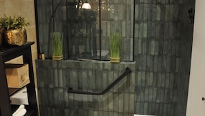 Un baño con inodoro, cabina de ducha de vidrio y repisa con toallas y plantas.