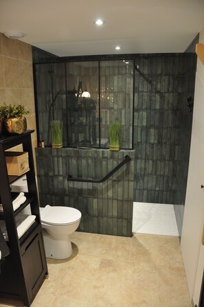 Een badkamer met een toilet, een douchecabine van glas en een plank met handdoeken en planten.
