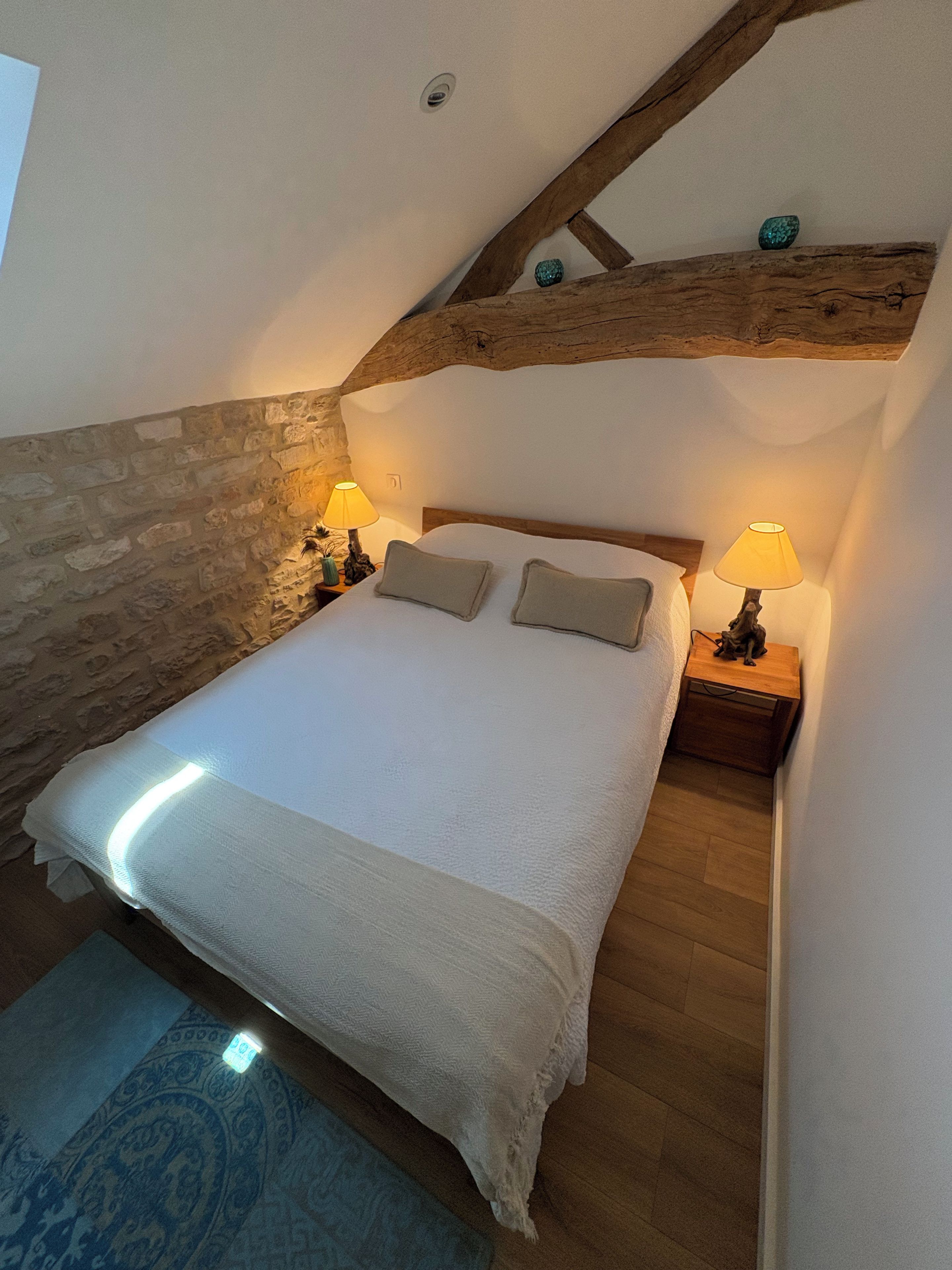 A bedroom with a sloped ceiling, a bed with a white duvet, two bedside lamps, and a wooden headboard.