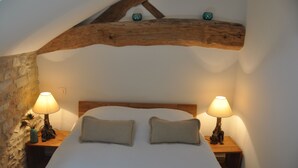 Un dormitorio con techo de madera, dos lámparas de noche, una cama con dos almohadas y una pared de piedra.