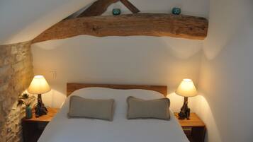 A bedroom with a wooden ceiling, two bedside lamps, a bed with two pillows, and a stone wall.