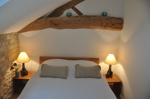 Een slaapkamer met een houten plafond, twee bedlampen, een bed met twee kussens, en een stenen muur.