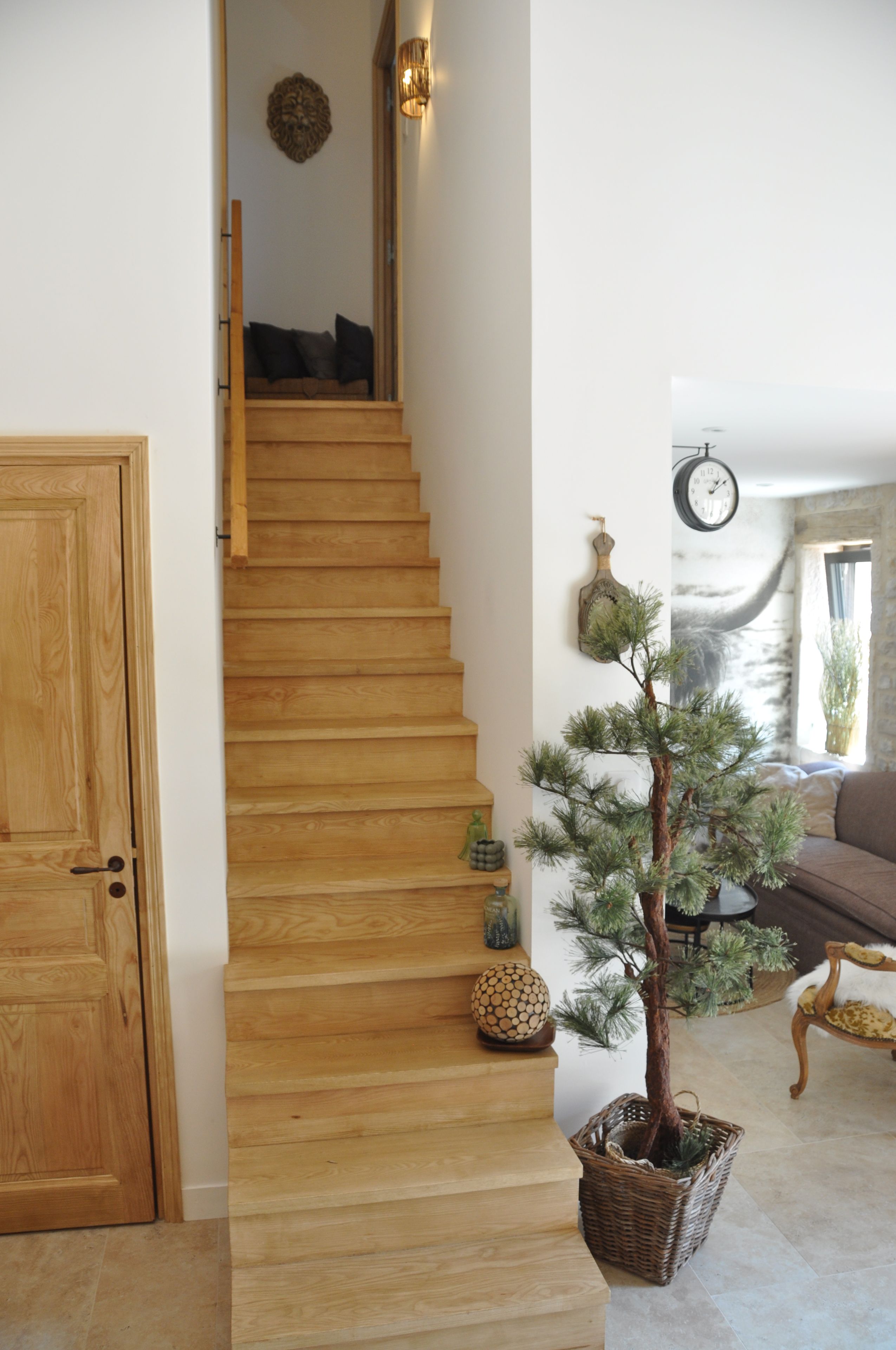 A wooden staircase leading to a living area with a pine tree, a clock, and a door.
