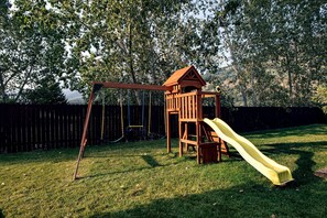 Eine Holzspielanlage mit Rutsche und Schaukeln in einem grünen Hinterhof.