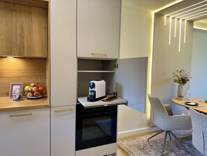 A modern kitchen with a built-in oven, a coffee machine, and a small dining area with a chair and table. - Newly renovated Berggold Chalet with the Chiemgau Card in the heart of Chiemgau (Siegsdorf)