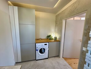 Ett litet och praktiskt tvättrum med en tvättmaskin, ett torkställ och en liten arbetsbänk med en växt.