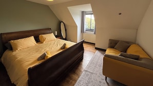 Un dormitorio con una cama, una silla, un espejo y una ventana.