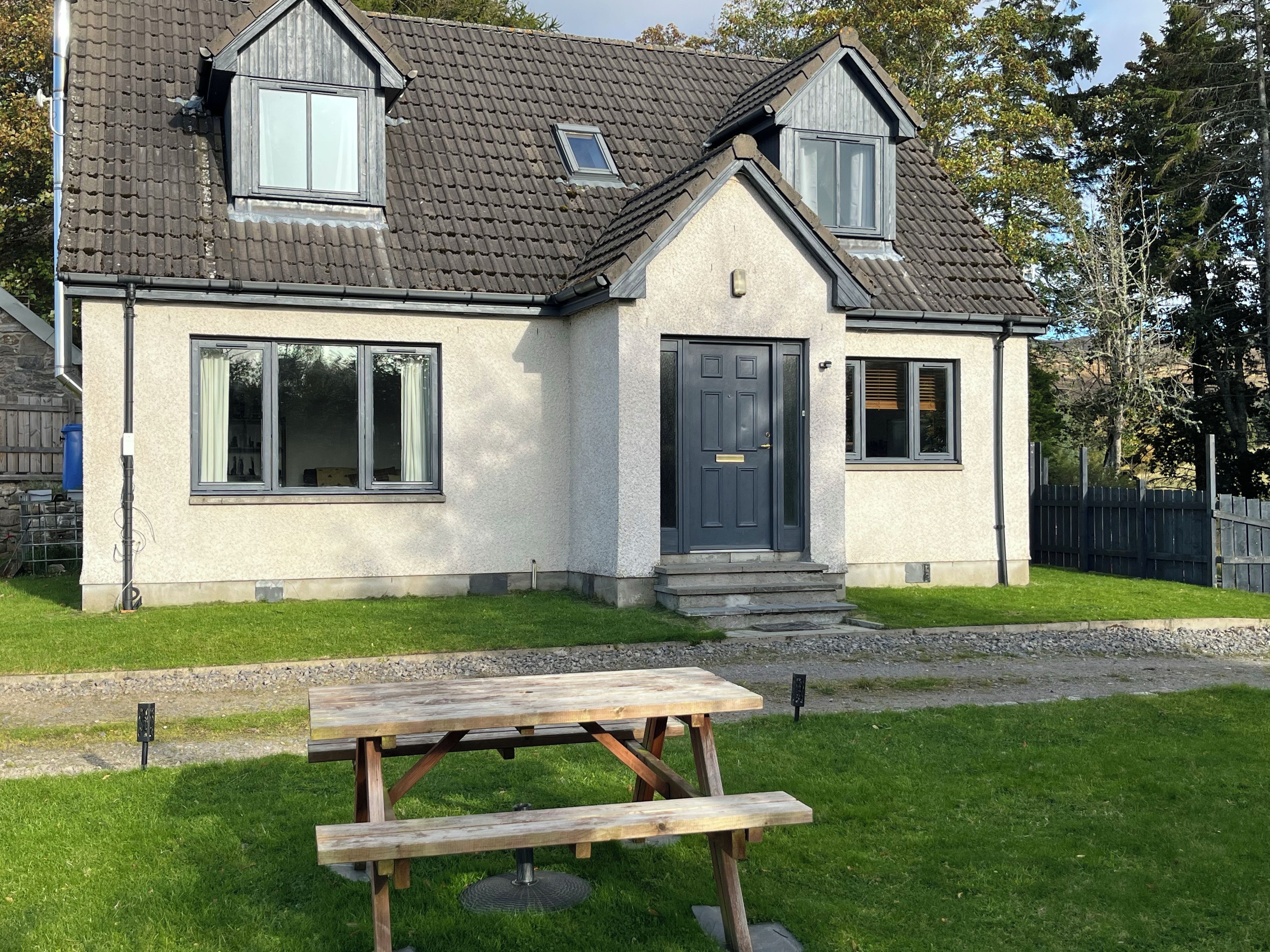 A two-story house with a grey door, a front porch, and a picnic table in the front yard.
