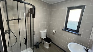 Un baño con ducha envuelta en vidrio, inodoro, lavamanos y ventana.