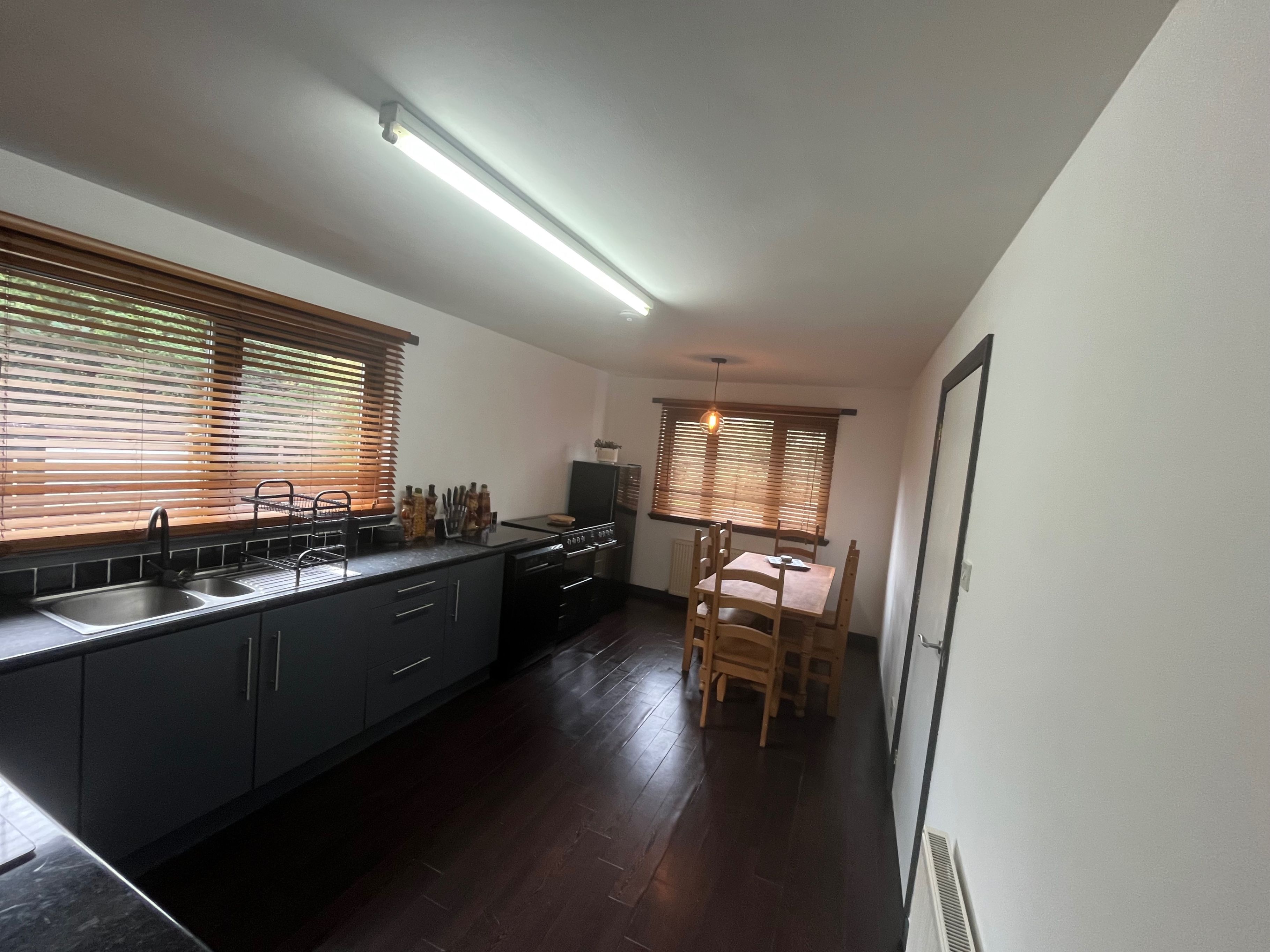 Cozinha moderna com armários escuros, pia de aço inoxidável e venezianas de madeira nas janelas.