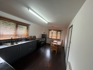 Cozinha moderna com armários escuros, pia de aço inoxidável e venezianas de madeira nas janelas.