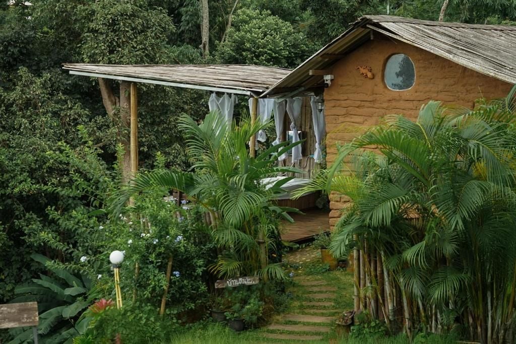 Uma cabana rústica de madeira com telhado de palha, cercada por vegetação exuberante e um deck de madeira.