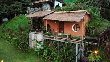 Una casa rústica con techo de paja, una ventana circular y una terraza de madera.