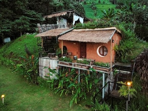 A rustic house with a thatched roof, a circular window, and a wooden deck.