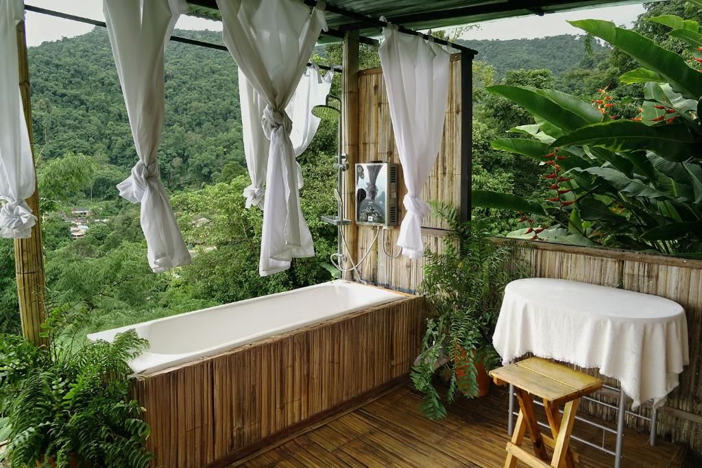 A wooden deck with a bathtub, a small table, and a view of a lush forest.