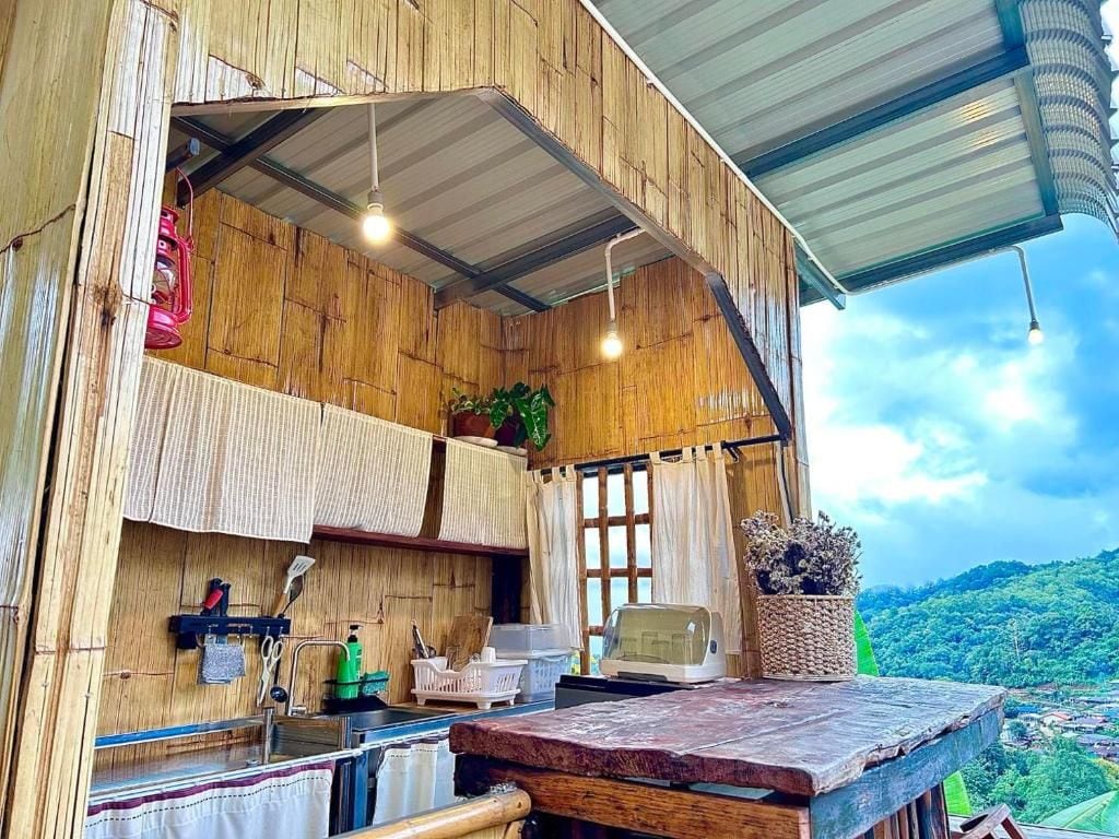 A rustic kitchen with wooden walls, a window, and a view of a green landscape.